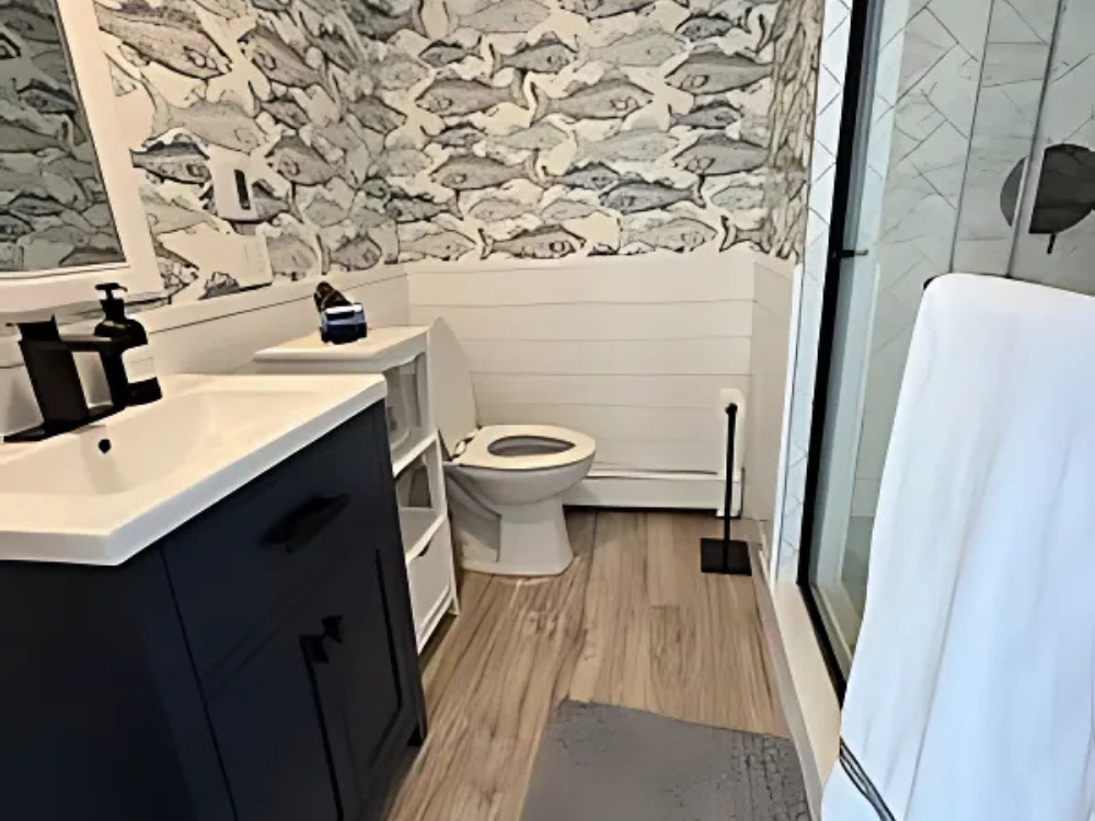 Modern bathroom renovation featuring wood-look flooring, black vanity, and unique fish-patterned wallpaper.