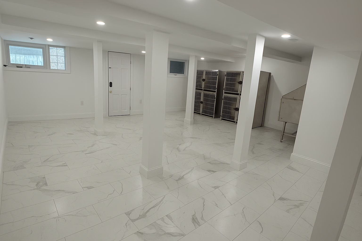 Finished basement with white marble-style tile flooring, white walls, and modern lighting — clean and spacious basement renovation.