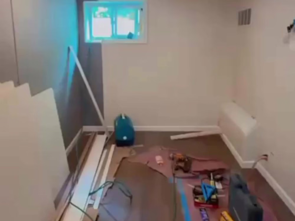 Room under renovation showing tools and materials for laminated flooring installation, with subfloor preparation and electrical setup in progress.