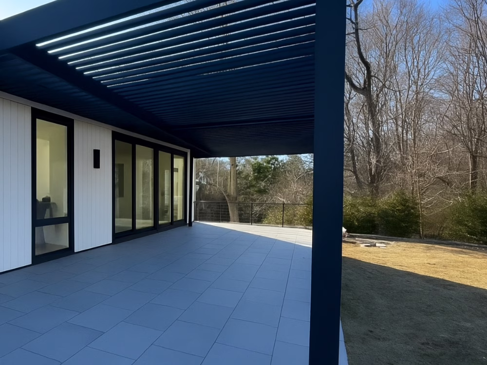 Modern Stone Patio Installation with sleek tiles and a stylish pergola, seamlessly connected to a contemporary home exterior.